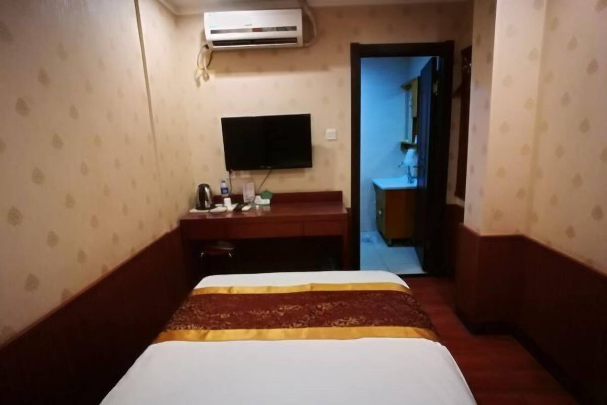 A hotel room with a bed, a desk, a television, and an air conditioning unit.