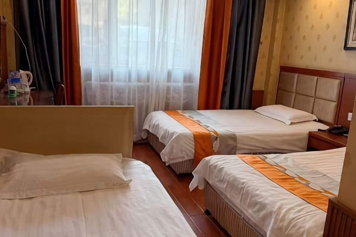 A hotel room with two beds, a wooden headboard, a radiator, and a window with sheer curtains.