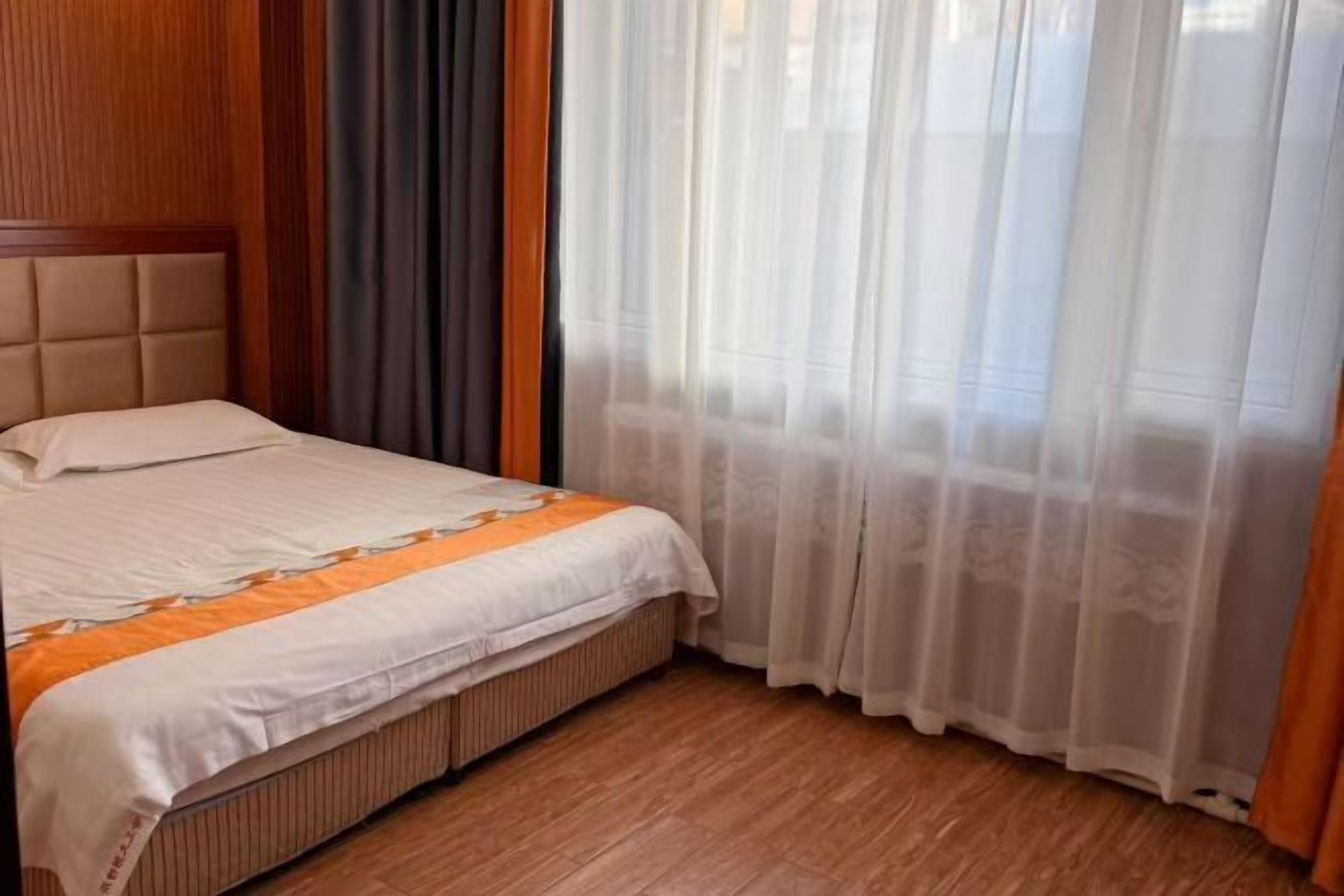 Ein Hotelzimmer mit Bett, Holz-Kopfstück und durchsichtigen Vorhängen.