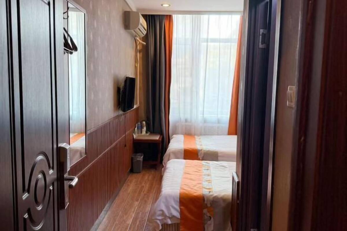 A hotel room with two beds, a wooden wardrobe, a small desk, a television, and a window with curtains.