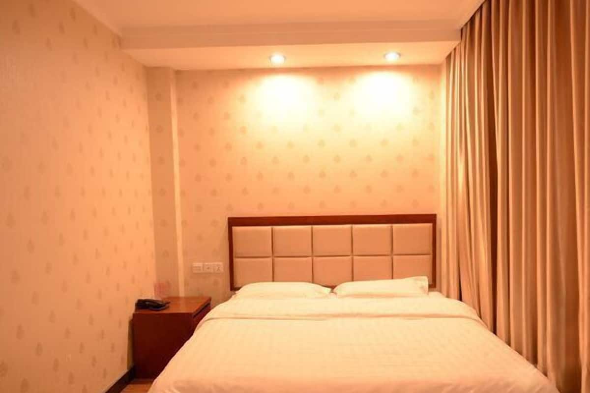 A hotel room with a bed, nightstand, and curtains.