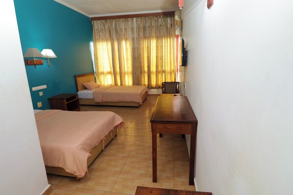 Habitación de hotel con dos camas, una mesa de madera, una silla, un televisor y una lámpara.