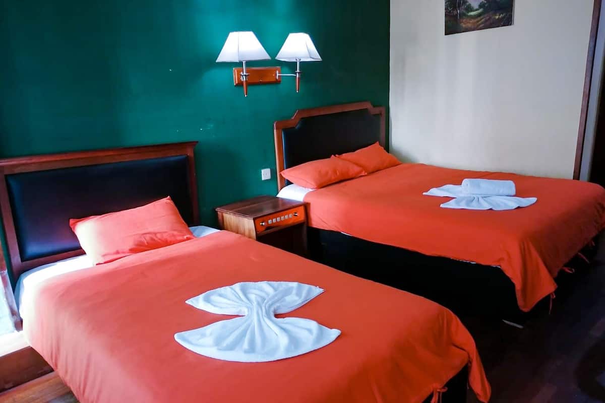 Dos camas con ropa de cama roja a juego y almohadas decorativas blancas, una mesita de noche y lámparas de pared.
