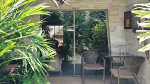 A patio area with wicker chairs and a table, surrounded by potted plants and a glass door leading to an indoor space. - LePrive Resort (Pattaya)