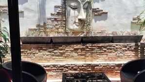 A stone wall with a decorative face, a small table, and wicker chairs. - LePrive Resort (Pattaya)