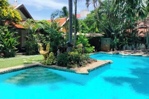 A swimming pool surrounded by lush greenery and a small building with a red roof. - LePrive Resort (Pattaya)
