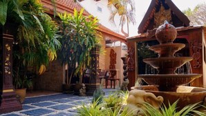 A courtyard with a stone fountain, potted plants, and traditional statues. - LePrive Resort (Pattaya)