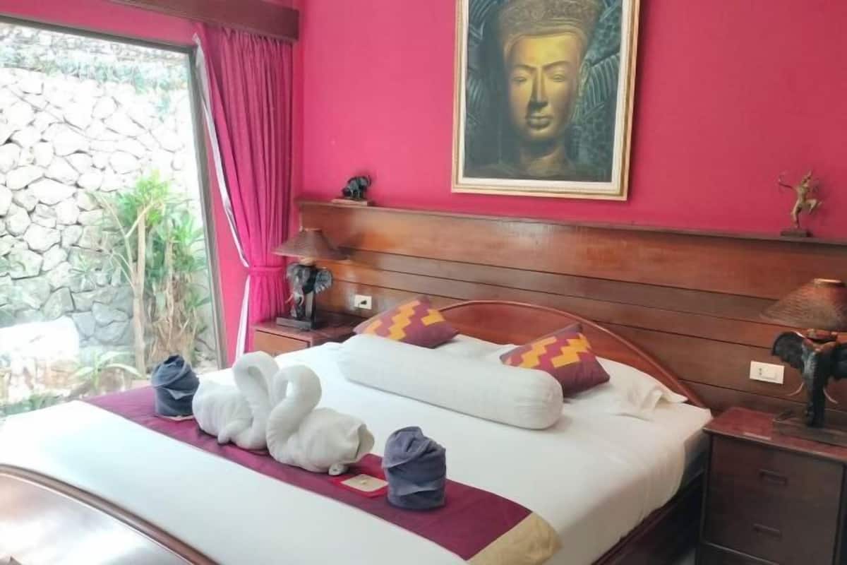 Quarto de hotel com cama, pintura de Buda, parede de pedra e janela com cortinas.