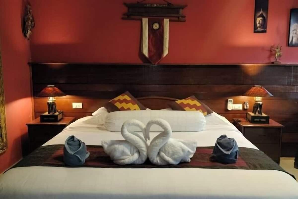 Quarto de hotel com uma cama grande, duas mesas de cabeceira e uma parede vermelha.