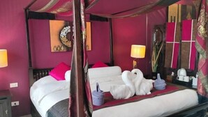 A four-poster bed with white linens and pink pillows, a bedside table with a lamp, and a mirror with decorative elements on the wall. - LePrive Resort (Pattaya)