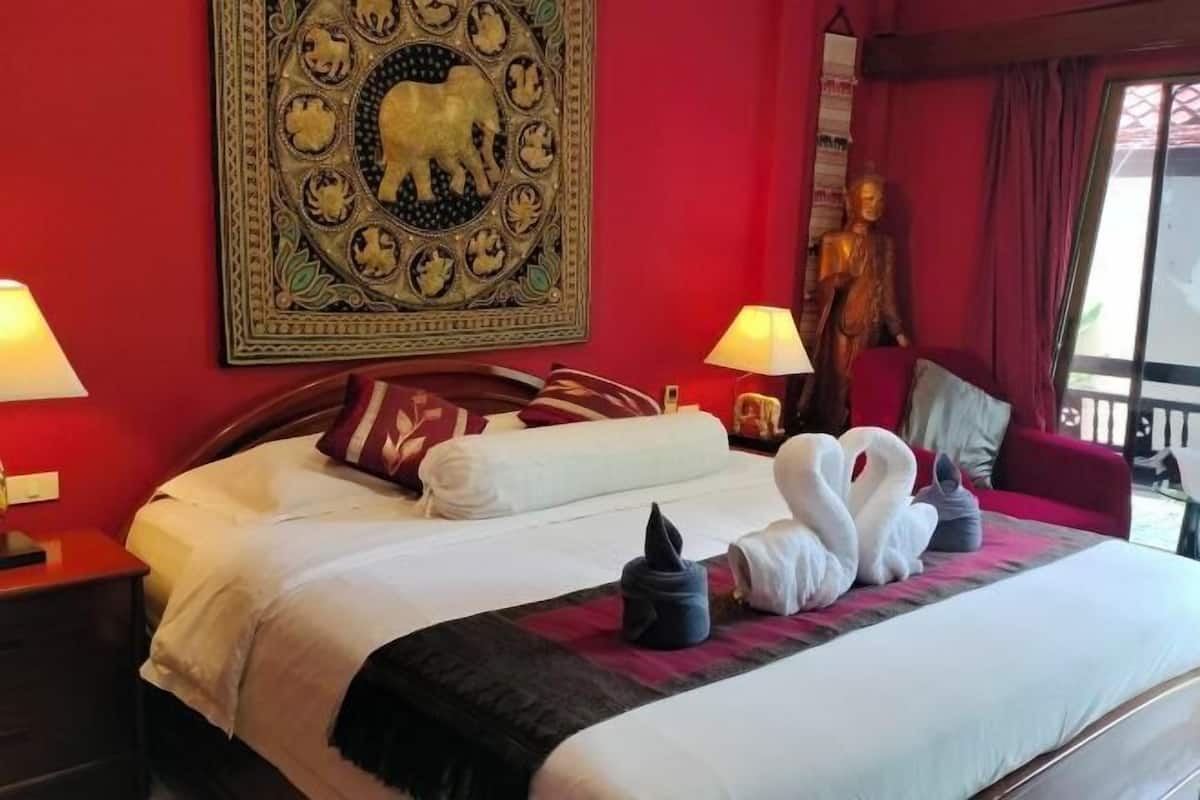 Quarto de hotel com cama grande, duas luminárias de cabeceira, um painel decorativo e uma estátua.