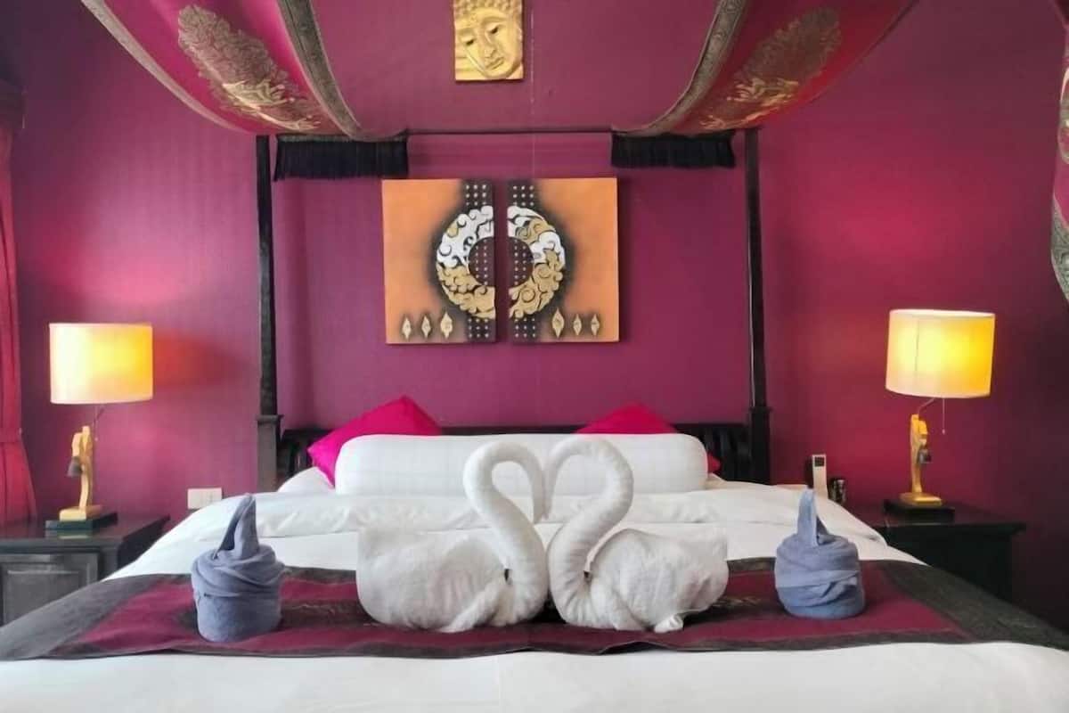 Quarto de hotel com uma cama, duas luminárias, um ornamento na parede e dois travesseiros em forma de cisne.