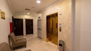 Una hall d'albergo con una reception, due porte, un cestino e una parete in marmo.