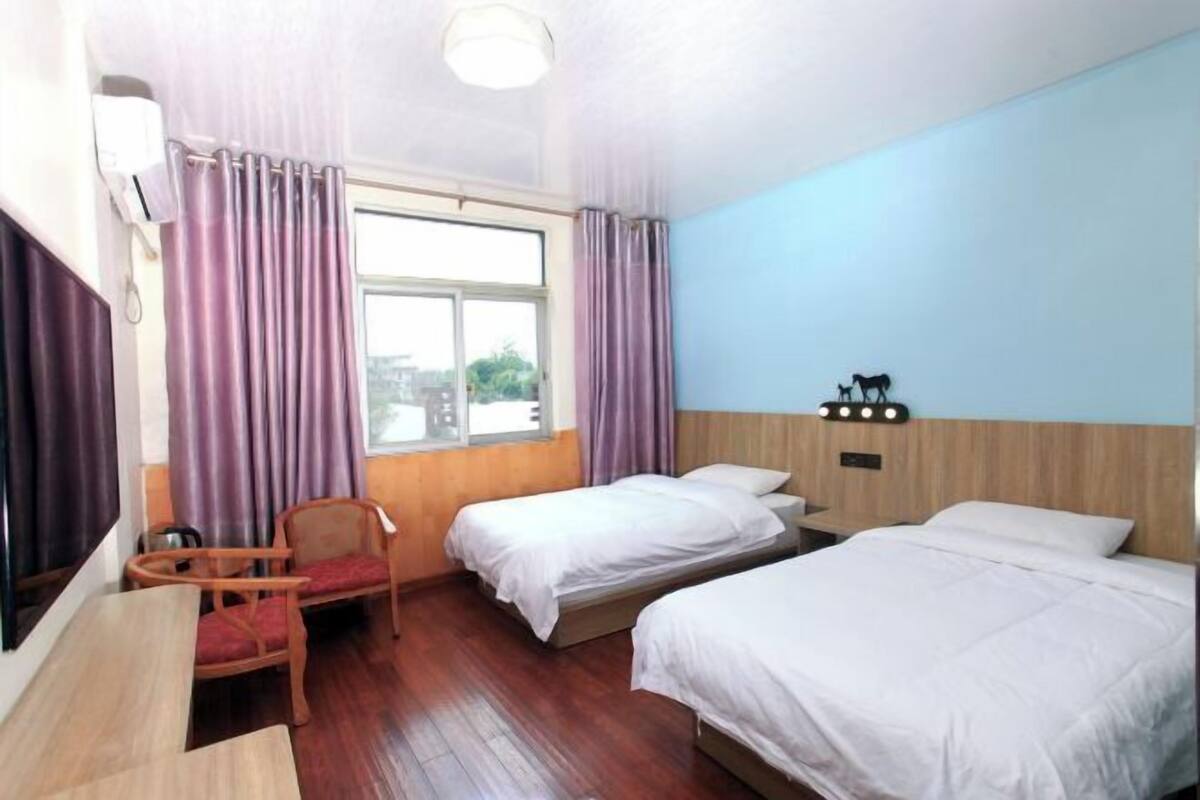 A hotel room with two beds, a chair, a table, and a window with curtains.
