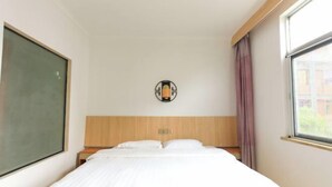 A hotel room with a bed, a nightstand, a wall-mounted light fixture, and a window with curtains. - ChunHui Inn Hotel (Wuyishan)