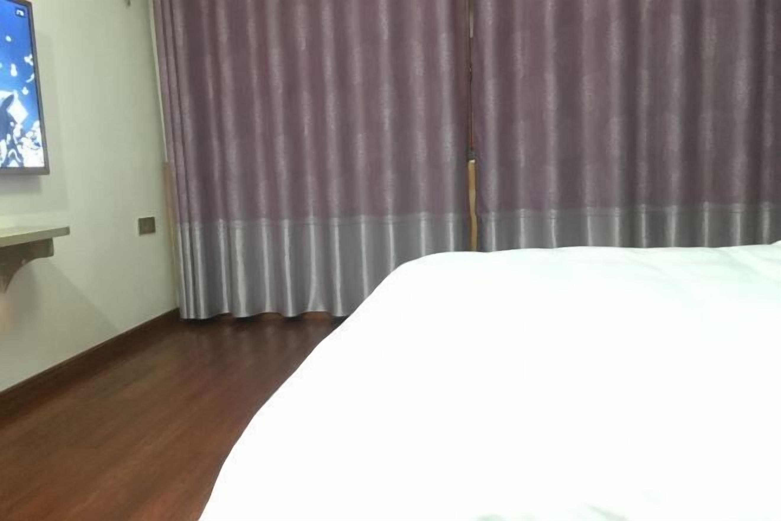 A hotel room with a bed, a wall-mounted TV, and a window with curtains.