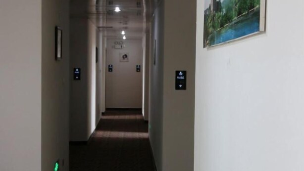 A hotel hallway with a carpeted floor, a framed picture on the wall, and directional signs. - ChunHui Inn Hotel (Wuyishan)
