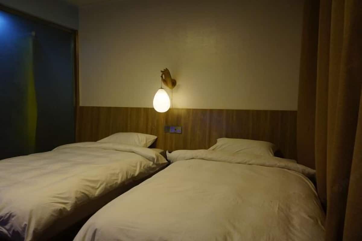 A hotel room with two beds, a wall-mounted light fixture, and a wooden headboard.