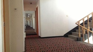 A hotel hallway with a carpeted floor, a staircase with wooden railings, and a plain wall. - ChunHui Inn Hotel (Wuyishan)