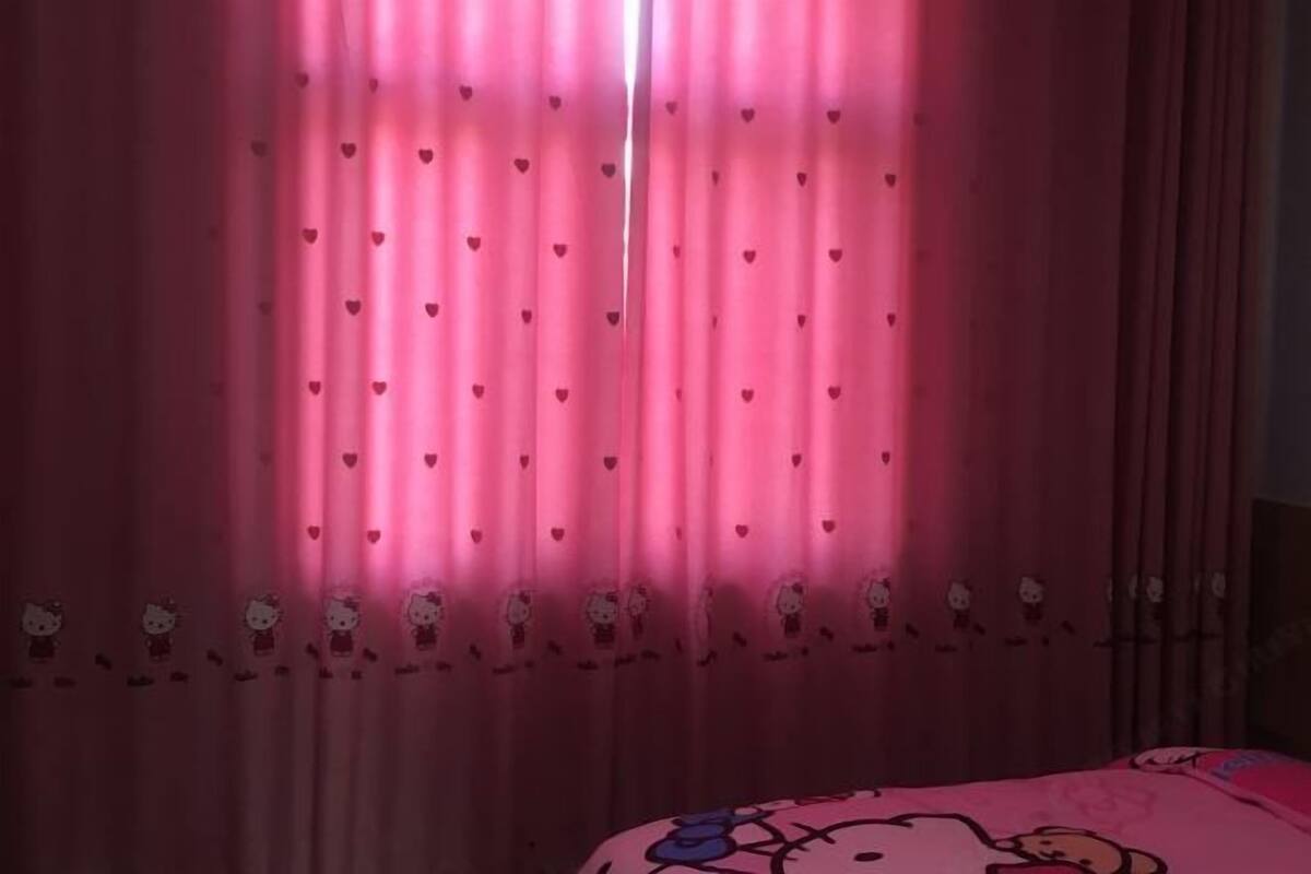 A room with pink curtains featuring heart patterns and Hello Kitty designs, a bed with a Hello Kitty-themed bedspread.
