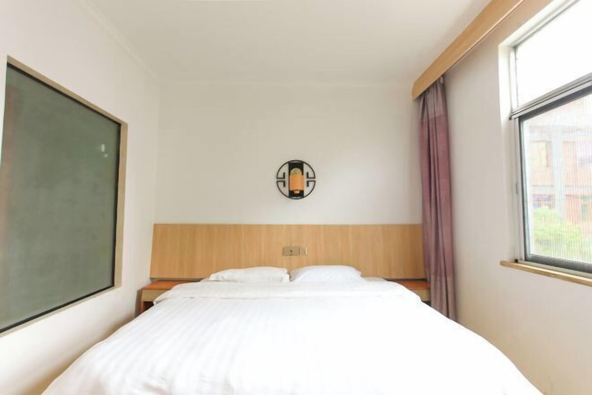 Habitació d'hotel amb llit, taulell de nit, llum penjada a la paret i finestra amb cortines.
