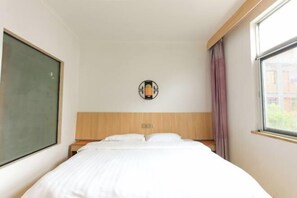 Habitació d'hotel amb llit, taulell de nit, llum penjada a la paret i finestra amb cortines.