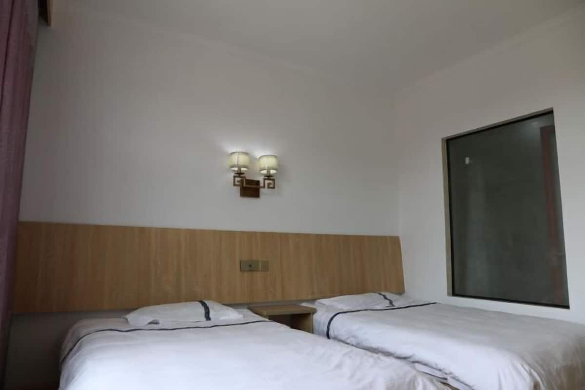 A hotel room with two beds, a wooden headboard, a wall-mounted light fixture, and a large window.