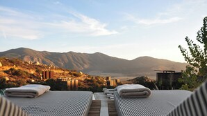 Une terrasse sur le toit, dotée de chaises longues et offrant une vue sur les montagnes.