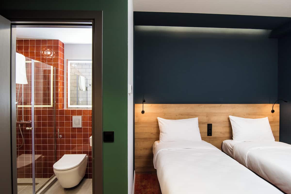 Une chambre d’hôtel avec une tête de lit en bois, deux lits, une douche et des toilettes.