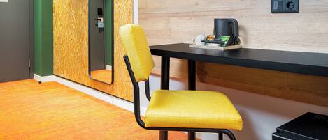 A modern hotel room with a yellow chair, a black desk, a television mounted on the wall, and a small black appliance on the desk.