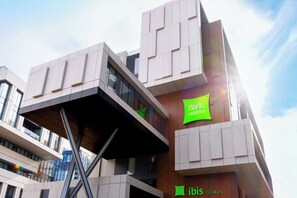 A modern building with a unique architectural design, featuring a prominent green sign with white text. - Ibis Styles Tbilisi Mziuri Park (Tbilisi)