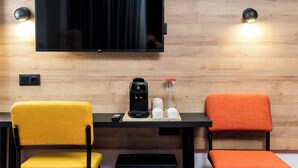 A modern room with a flat-screen TV mounted on the wall, a coffee maker, a water bottle, and two chairs. - Ibis Styles Tbilisi Mziuri Park (Tbilisi)