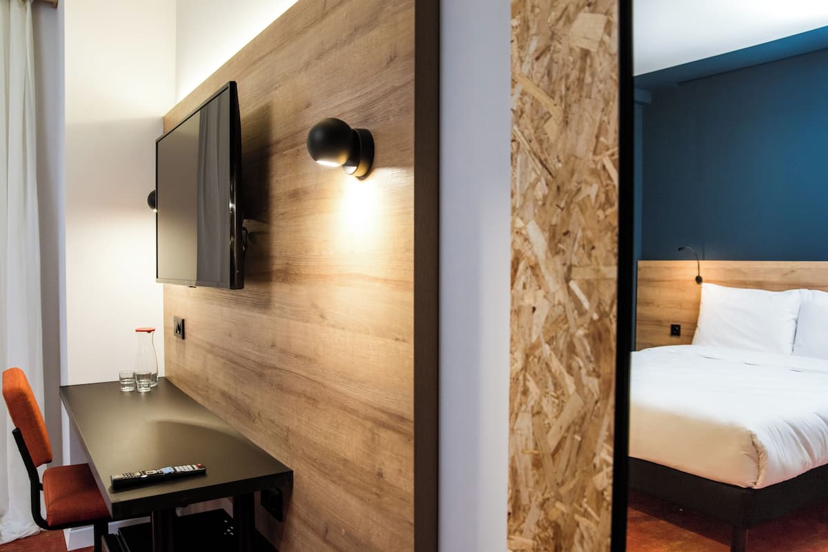 Une chambre d’hôtel avec un mur en bois, un téléviseur à écran plat fixé au-dessus d’une table, une télécommande et un lit avec une literie blanche.
