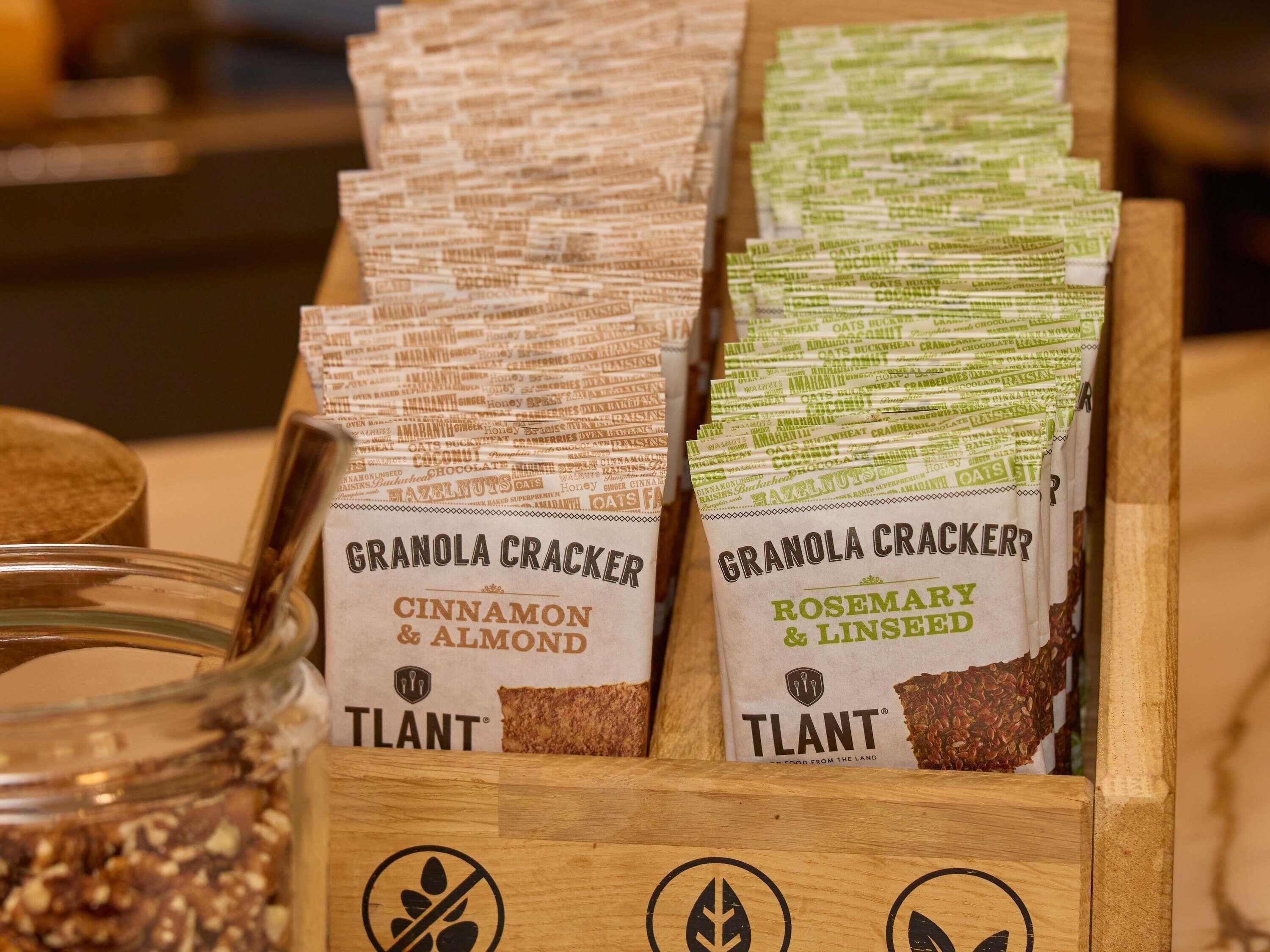 A wooden box containing two types of granola crackers, one with cinnamon and almond, and the other with rosemary and linseed, both branded by Tplant.