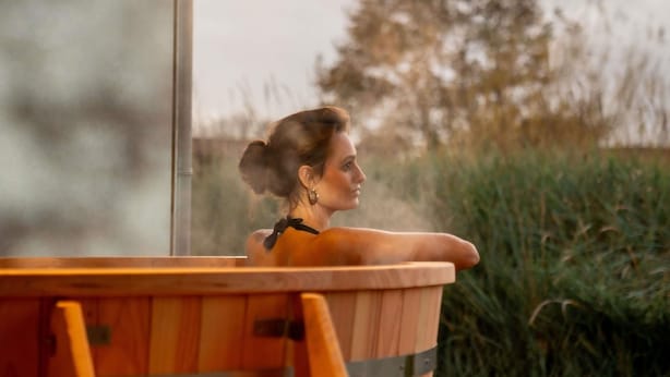 A person in a wooden tub with a view of a grassy field and trees. - Hotel Ter Zand - Handwritten Collection (Burgh-Haamstede)