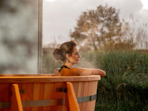 A person in a wooden tub with a view of a grassy field and trees. - Hotel Ter Zand - Handwritten Collection (Burgh-Haamstede)