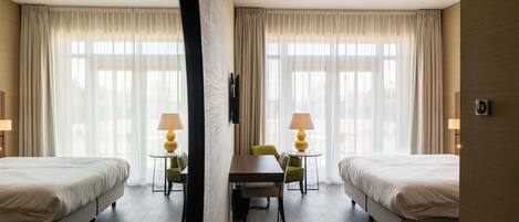 A hotel room with two beds, a dining table, chairs, lamps, and a TV.