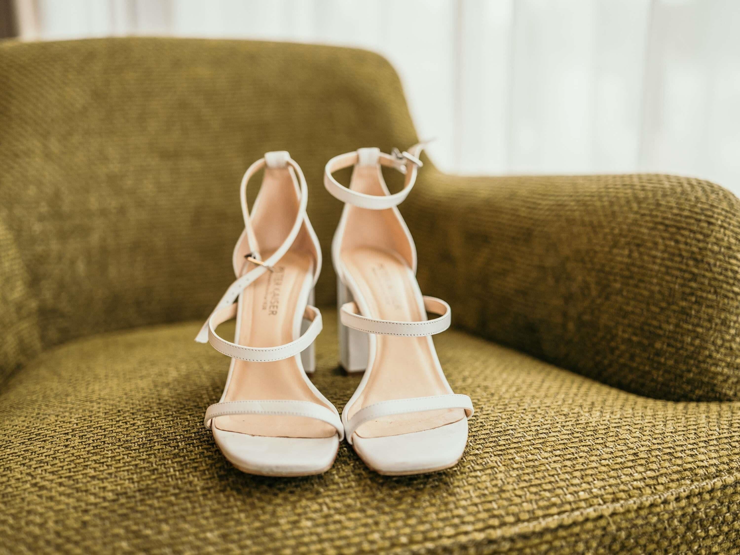 A pair of white high-heeled shoes with ankle straps on a textured green sofa.