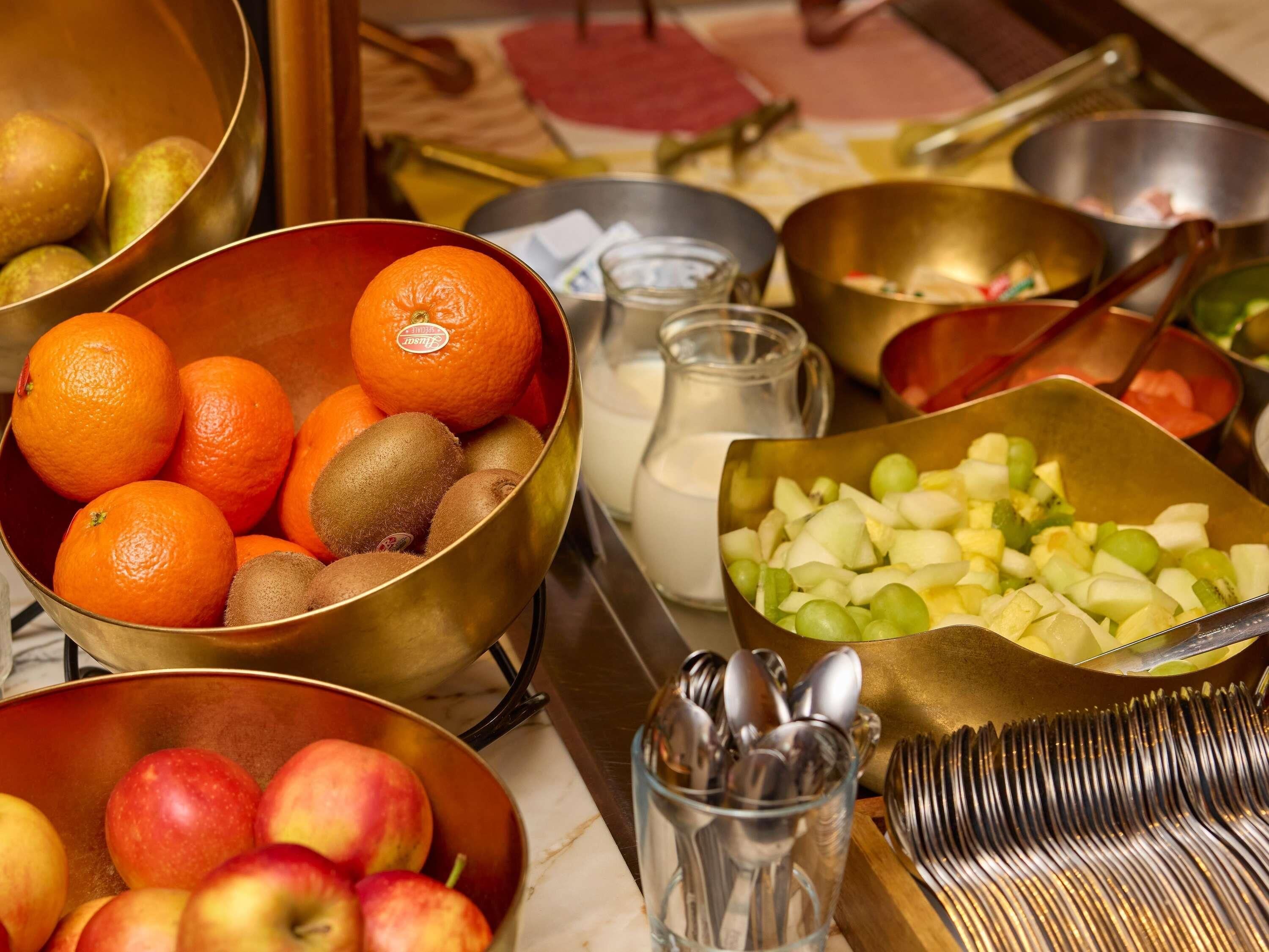 A kitchen counter with bowls of fruits, a milk jug, and utensils.