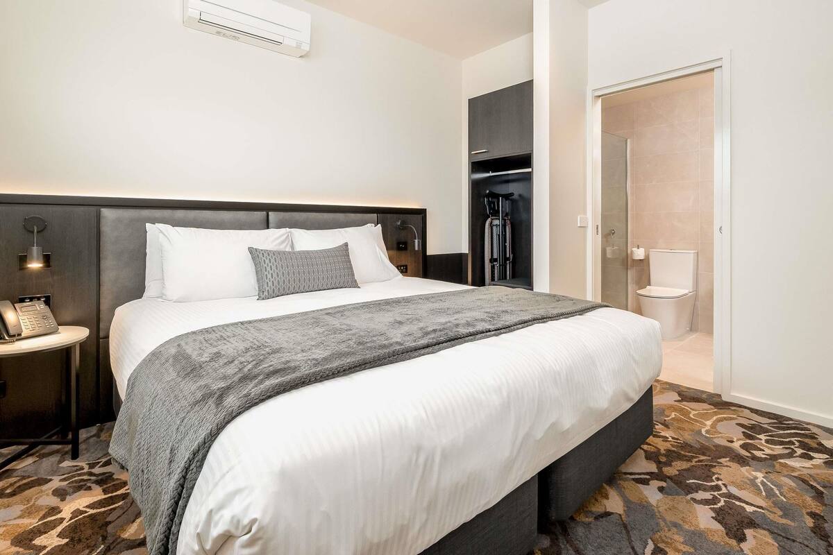 A hotel room with a bed, bedside table, lamp, and a closet with a mirror.