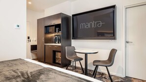 A modern hotel room with a bed, a small kitchenette, a seating area with two chairs, and a TV mounted on the wall. - Mantra Shepparton (Shepparton)