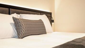 A neatly made bed with white linens and a patterned pillow.