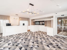 Una cocina moderna con armarios blancos, piso estampado geométricamente e iluminación colgante.