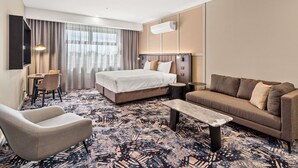 A hotel room with a bed, a sofa, a chair, a small table, and a desk with a lamp. - Mantra Shepparton (Shepparton)