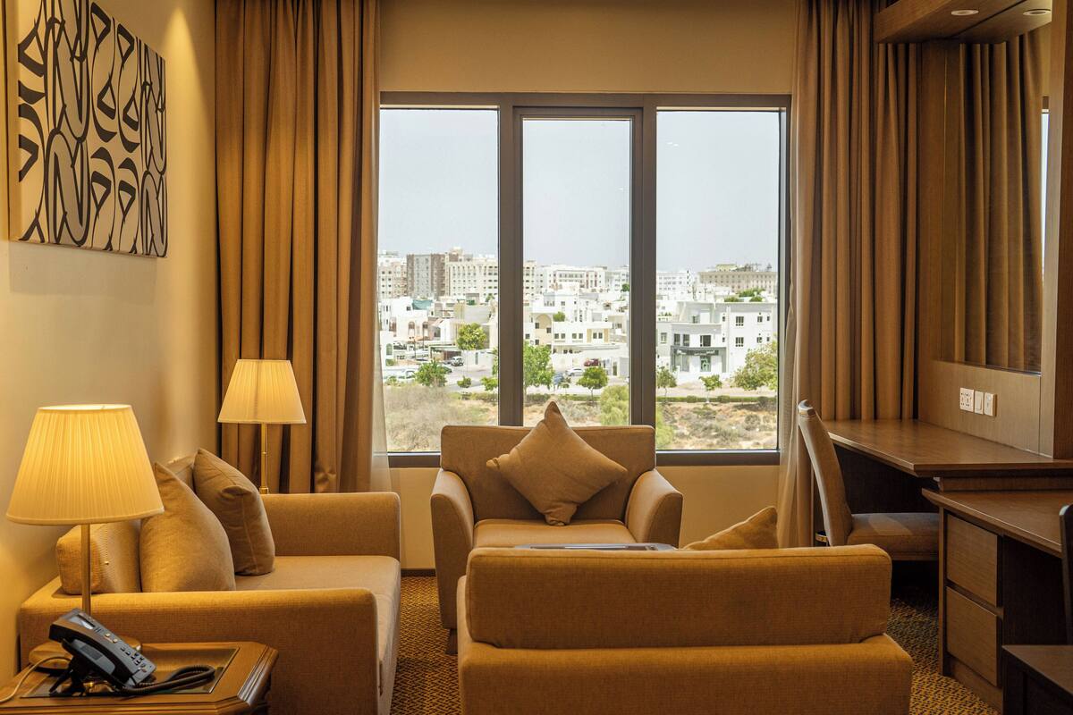 Une chambre d’hôtel avec une grande fenêtre, un canapé, un bureau et une lampe.