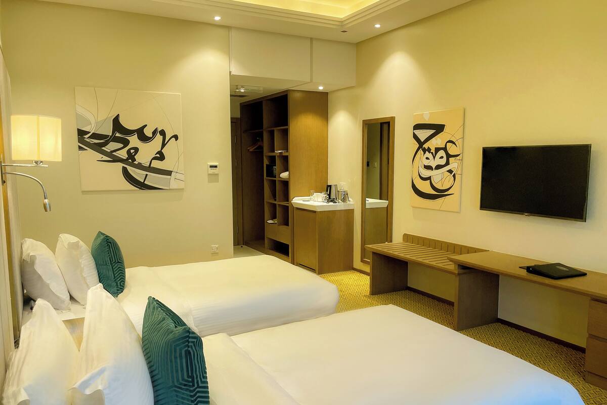 Une chambre d’hôtel avec deux lits, un bureau, une télévision et des œuvres d’art accrochées aux murs.