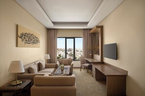 A hotel room with a sofa, armchair, coffee table, desk, and a TV.