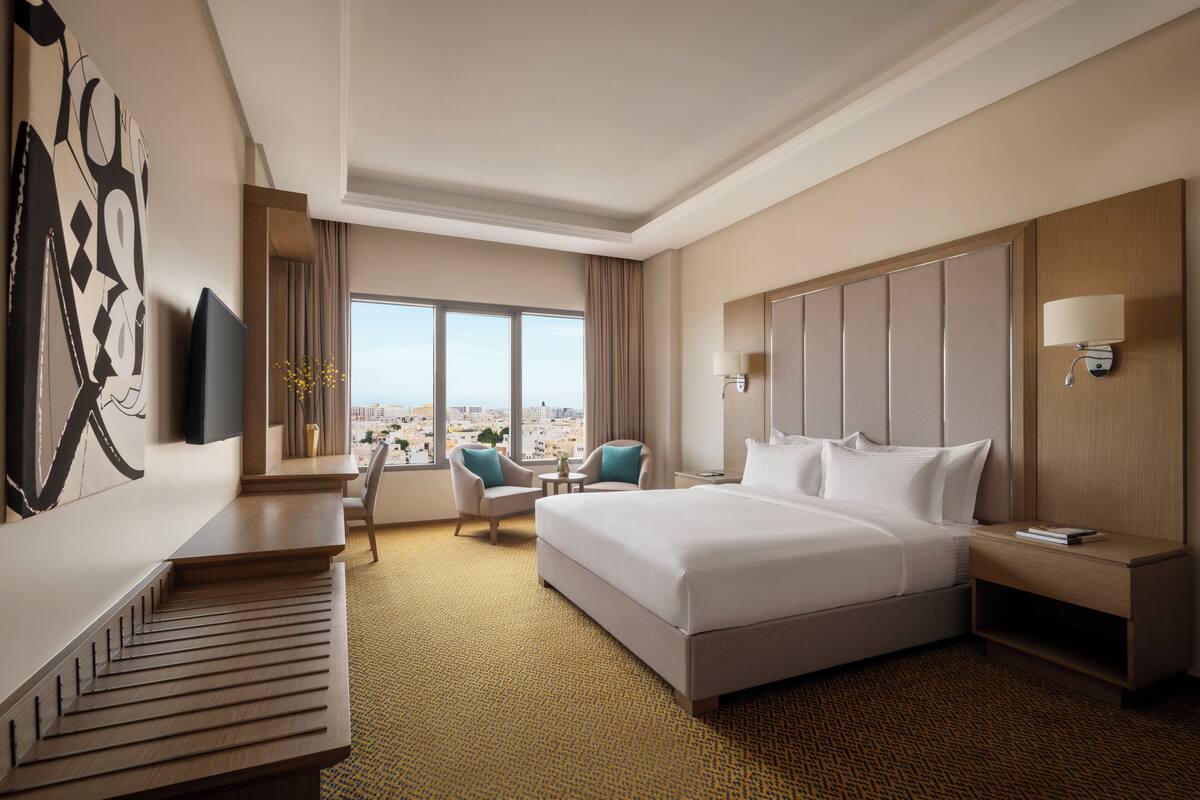 Une chambre d’hôtel avec un grand lit, un bureau, une chaise, une télévision et une vue sur la ville.