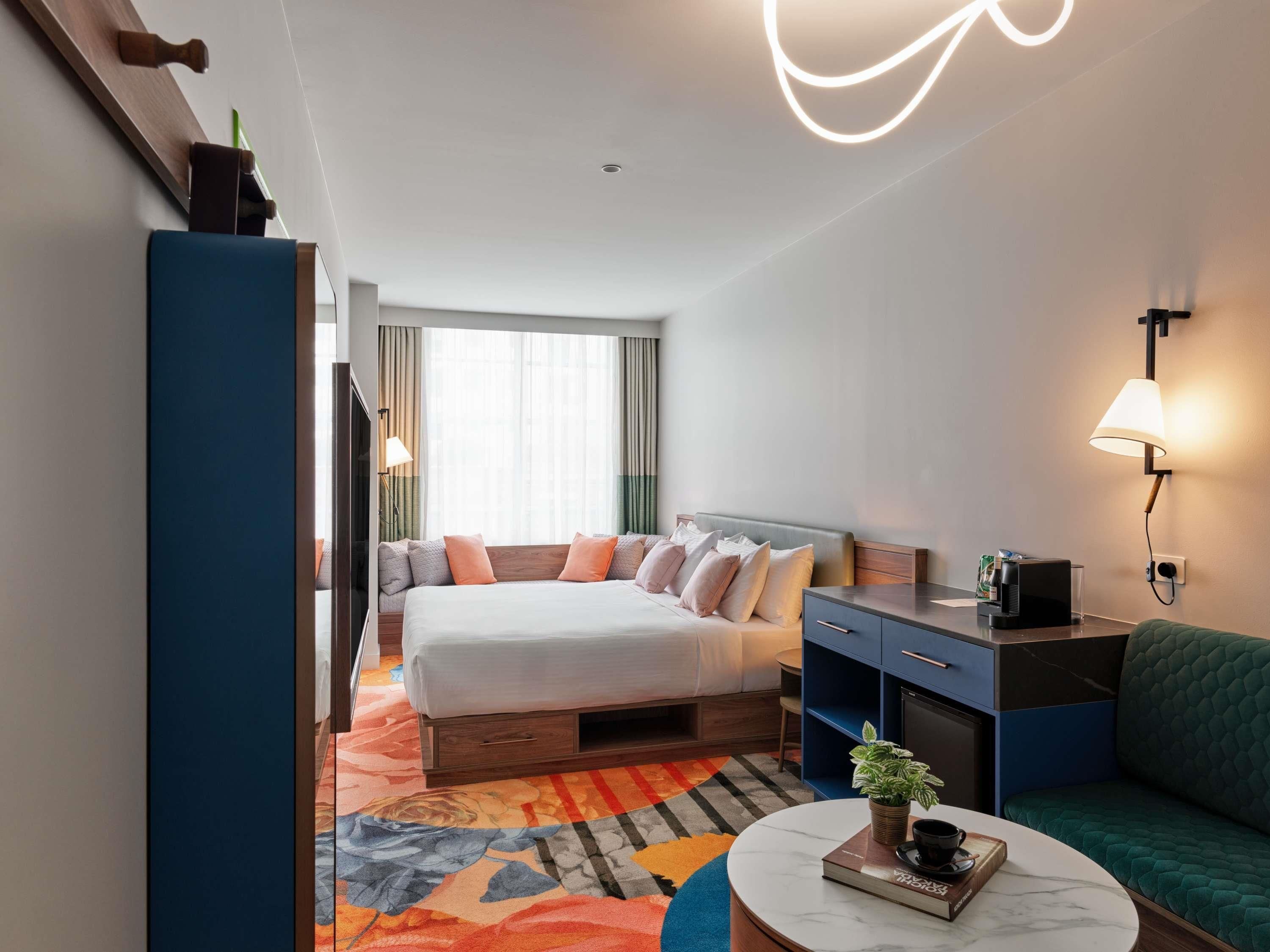 Een hotelkamer met een bed, een bureau, een bank, een koffiezetapparaat en een lamp.