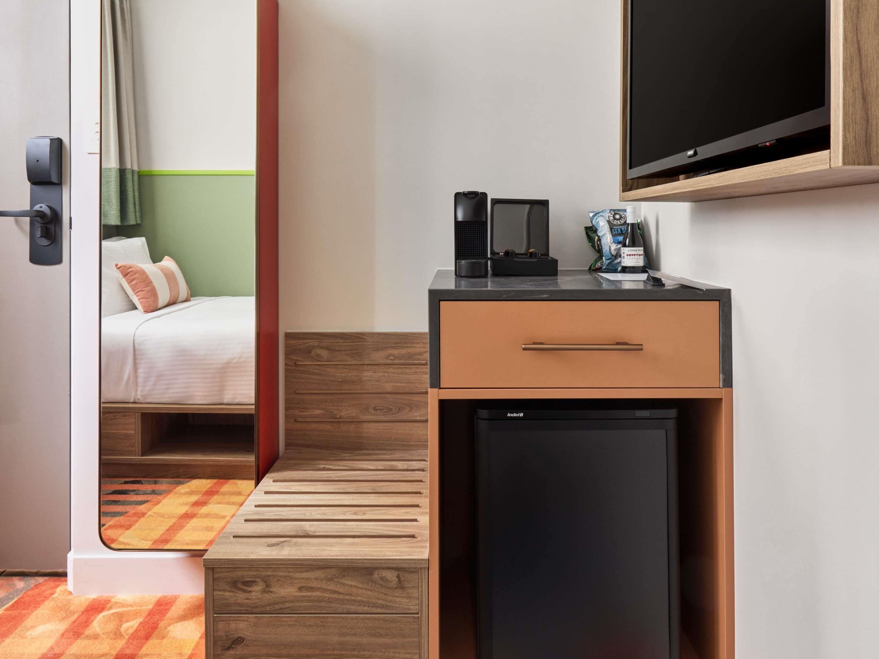 Una habitación de hotel con cama, escritorio con cafetera, televisor y minibar.